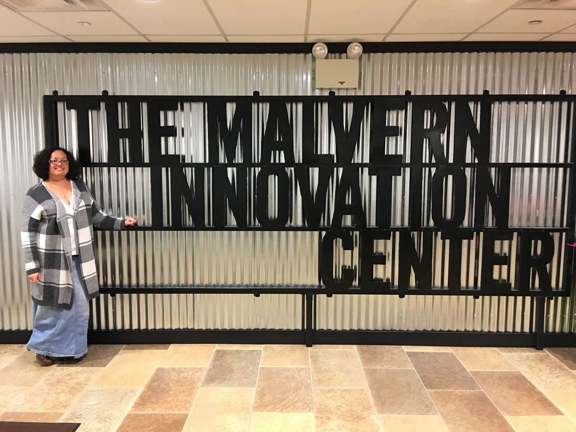 Person standing next to 'The Malvern Innovation Center' sign on a corrugated wall.