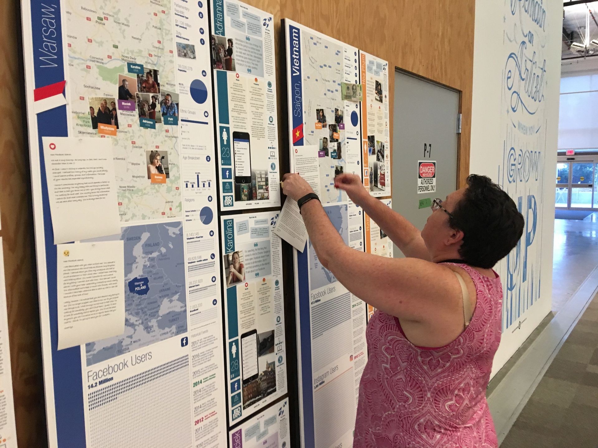 Woman reading and adjusting informational posters on a wall inside a building.