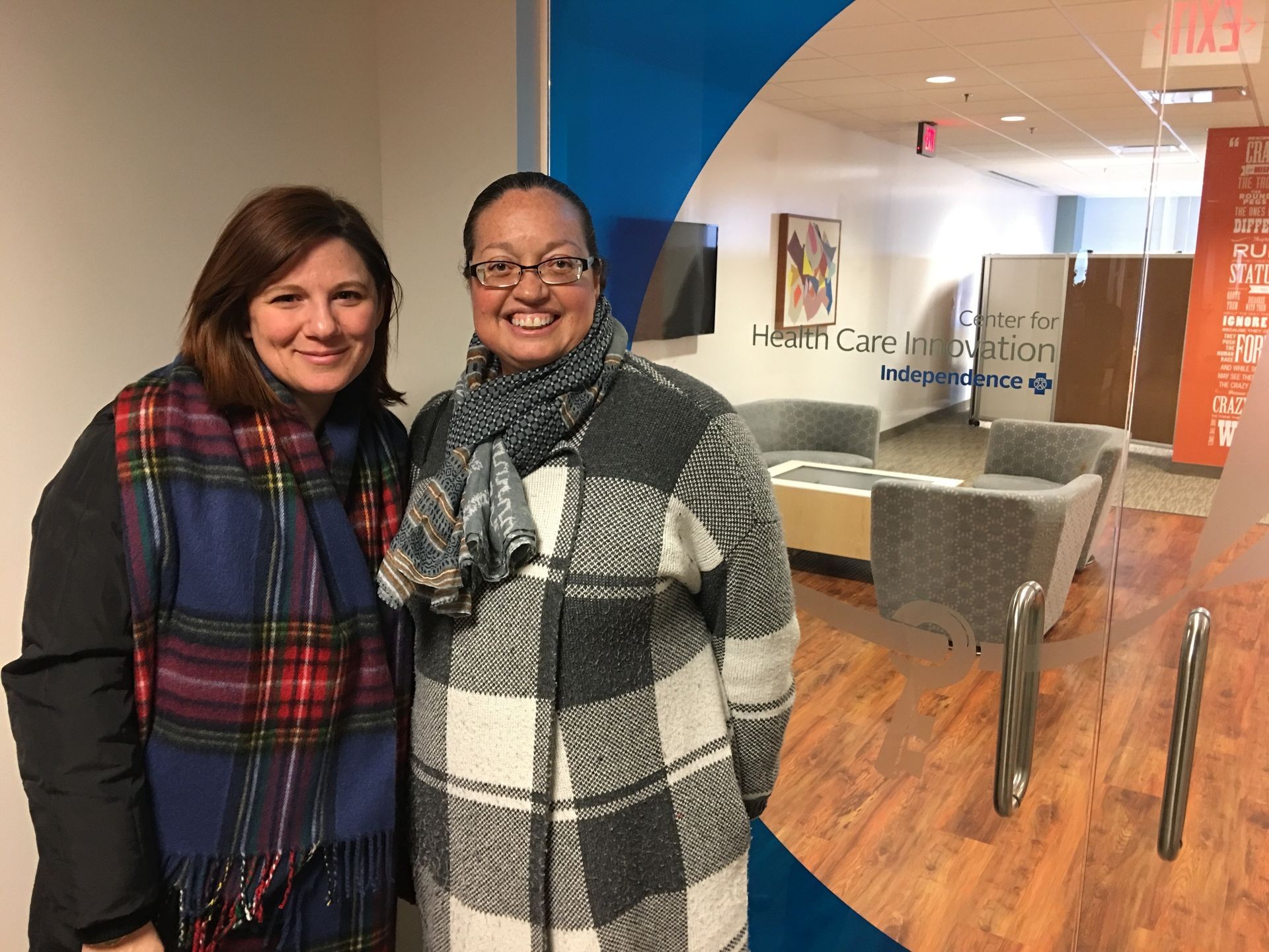 Two women wearing scarves smiling at the camera in front of the Center for Health Care Innovation office.